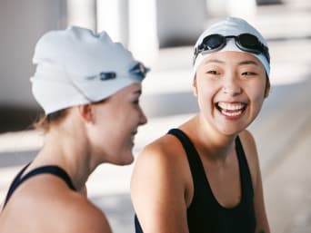 Schwimmen im Verein: Zwei Schwimmerinnen sitzen am Beckenrand und lachen miteinander.