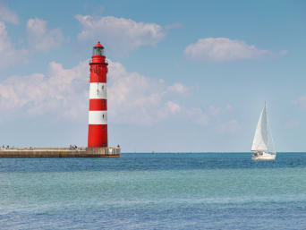 Zeilboot vaart op rustig zeewater in de buurt van een vuurtoren.