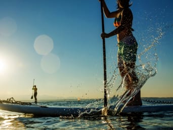 SUP – Twee personen peddelen in de zon op hun SUP-board over een meer. 