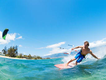 Cómo aprender kitesurf: un joven kitesurfista surfea cerca de la playa trazando una curva.
