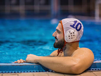 Unterwasserhockey Ausrüstung: Octopush-Spieler trägt Wasserballkappe und hält sich am Beckenrand fest.