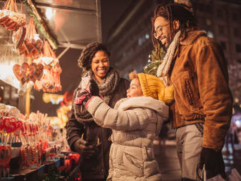 Beschäftigung Kinder Weihnachten: Familie steht an einem Lebkuchenstand auf einem Weihnachtsmarkt.