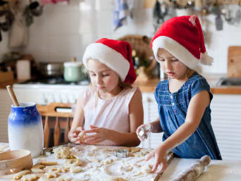 Kruche ciasteczka świąteczne – dwie dziewczynki w czapkach Mikołaja wykrawają ciasteczka.