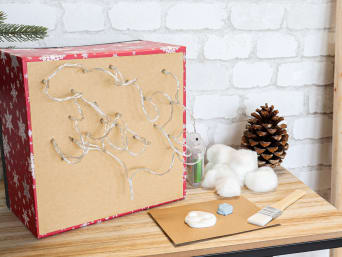 Kerstversiering voor kinderen - het bevestigen van de LED-kaarsverlichting voor het kerstlandschap in een kartonnen doos. 