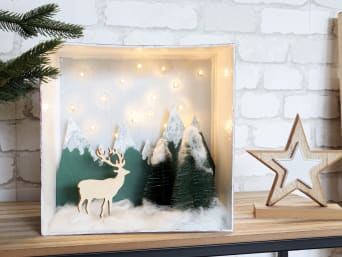 Transformez une boîte inutilisée en une jolie décoration de Noël. Ici, un paysage d’hiver avec un ciel étoilé et des arbres enneigés.