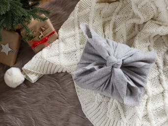 Weihnachtsgeschenke mit der Furoshiki-Methode in einem quadratischen Tuch einpacken