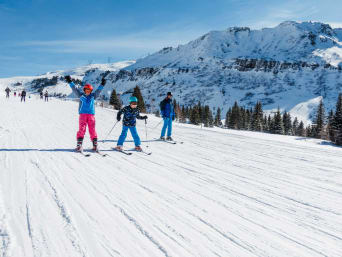 Skiferien Schweiz: Familie auf Skiern fährt einen schneebedeckten Hang herunter.
