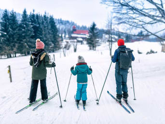Langlauf Österreich: Familie auf Skiern betrachtet die verschneite Landschaft.