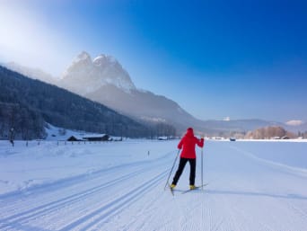 Langlauf Österreich: Langläuferin fährt durch den Schnee und blickt auf die Zugspitze.