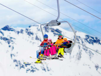 Vacanze sulla neve con bambini: famiglia sullo skilift pronta per sciare.