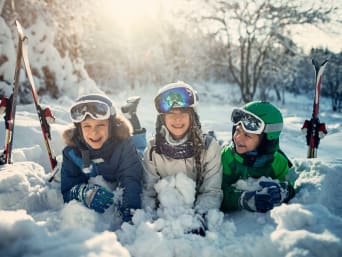  Wyjazd na narty z dziećmi: kilkuletnie, uśmiechnięte maluchy bawią się w świeżym śniegu.