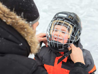 Eishockey Ausrüstung: Vater hilft seinem Sohn, den Helm für das Eishockey-Traning zu veschließen.