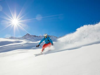 Sports d’hiver : une personne dévale une piste poudreuse en snowboard.