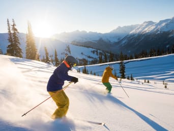 Schönste Skigebiete: Skifahrer fahren im Sonnenschein einen schneebedeckten Hang herunter.