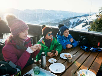 Meilleures stations de ski en France : une famille prend un goûter sur la terrasse d’un chalet.