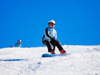 Snowboard dla dzieci – dziecko zjeżdża po stoku na desce snowboardowej.