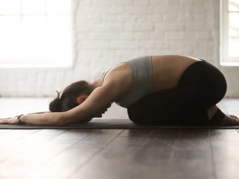 Frau in Balasana Yoga-Pose kniet auf einer Yoga-Matte.