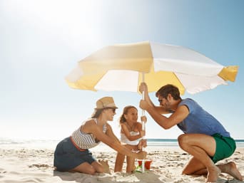 Sonnenschirm – Familie stellt einen Sonnenschirm am Strand auf