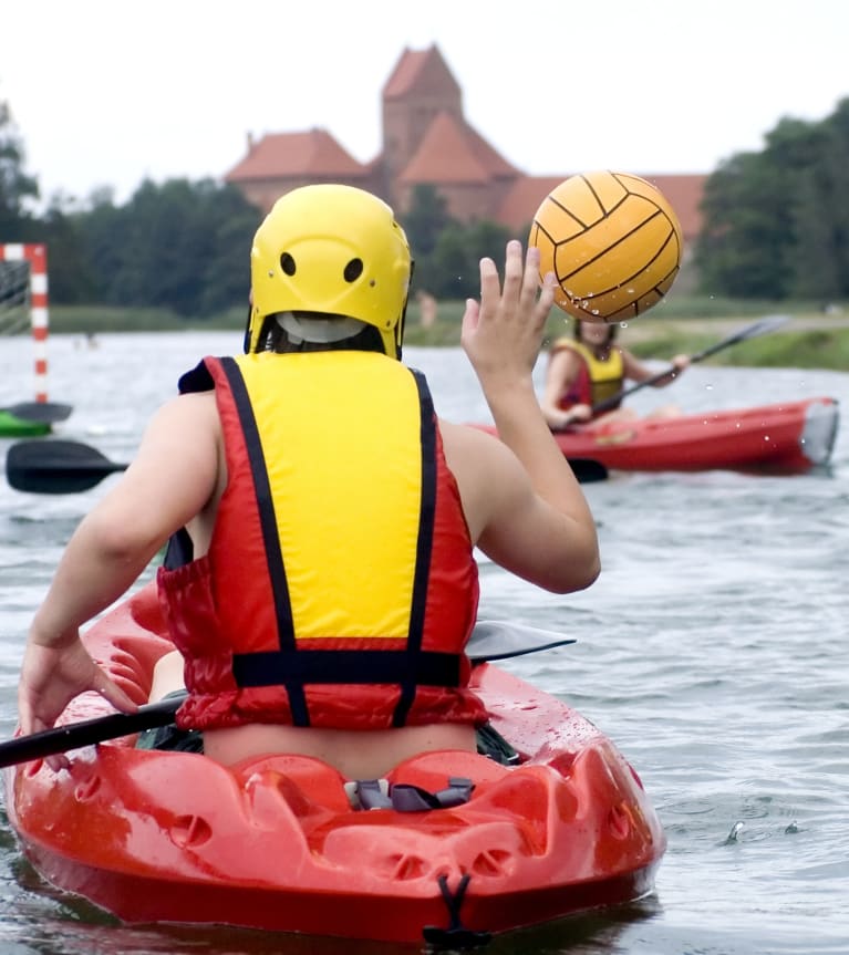 Teamsport op het water: kanopolospeler in rode kano vangt de bal tijdens een wedstrijd.