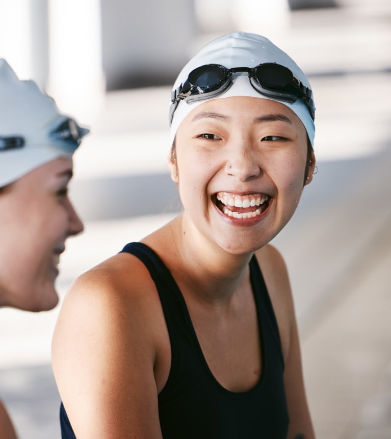 Mannschaftssport Wasser: Zwei Schwimmerinnen sitzen am Beckenrand und lachen miteinander.