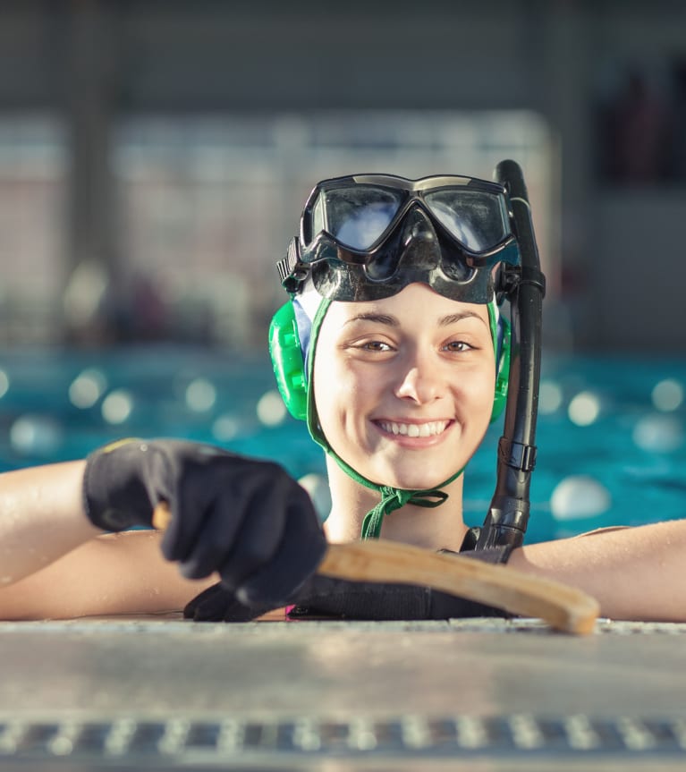 Mannschaftssport Wasser: Spielerin stützt sich am Beckenrand ab und hält ihren Schläger in die Kamera.