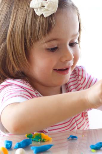 Cadeaus voor kinderdag: kleuter bewerkt kleurrijke boetseerklei op tafel. 