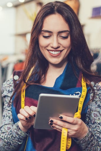 Guía de profesiones del mundo de la moda: una mujer con una tablet y una cinta métrica trabajando en una tienda de ropa.