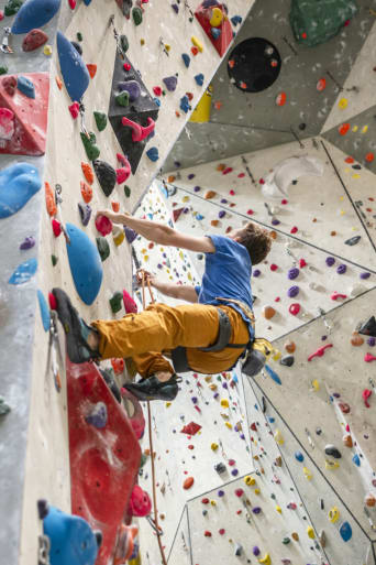 Deportes de escalada para adultos: un hombre escala la pared de un rocódromo.