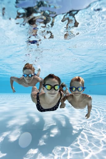 Sport per bambini: tre bambini con gli occhialini nuotano sul fondo della piscina.