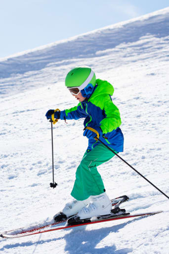Sporty zimowe dla dzieci – chłopiec na nartach zjeżdża po zaśnieżonym stoku.
