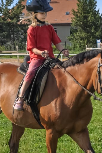 Paardrijden voor kinderen: een klein meisje rijdt met een paard over een grasveld. 