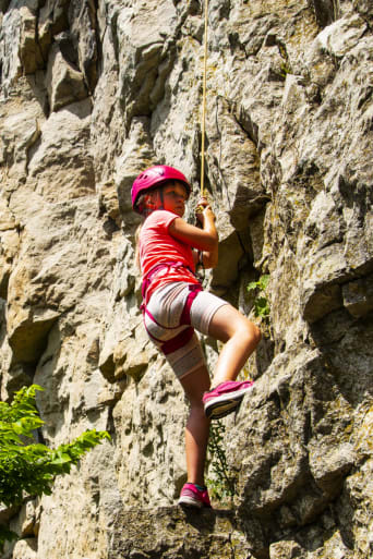 Wspinaczka górska dla dzieci – dziewczynka wspina się na skałę.