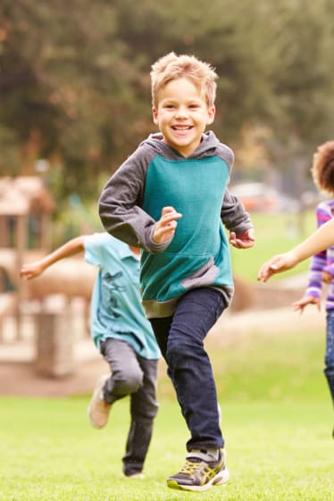 Sport für Kinder: Eine Gruppe von Kindern läuft lachend über eine Wiese. 