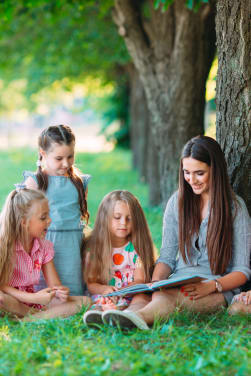 Leren lezen: leerkracht leest met kinderen in het park.