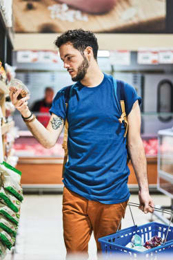 Un jeune homme fait ses courses au supermarché et compare les prix des produits pour économiser.