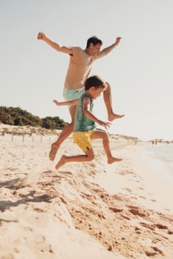Dove andare in vacanza con i bambini: un papà e un bambino saltano sulla sabbia in Sardegna.