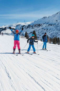 Langlauf Österreich: Familie auf Skiern fährt einen schneebedeckten Hang herunter.