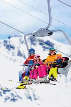 Winterurlaub mit Kindern: Familie fährt mit einem Skilift den Berg hinauf.