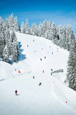 Günstiger Skiurlaub: Skifahrer fahren schneebedeckte Piste herunter.
