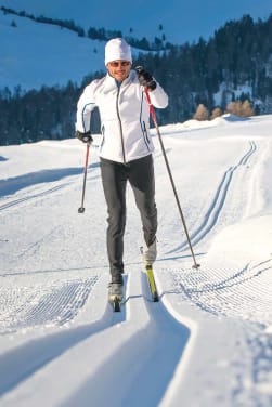 Die schönsten Langlaufgebiete in der Schweiz: Langläuferin fährt durch Schnee.