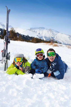 Skifahren Regeln: Familie liegt im Schnee und lacht in die Kamera.