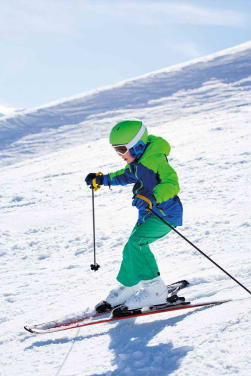 Kinder Skifahren: Junge auf Skiern fährt einen schneebedeckten Hang herunter.