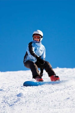 Snowboard Kinder: Junges Mädchen fährt auf ihrem Snowboard einen Hang herunter.