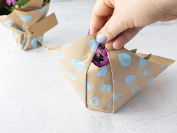 Cadeau DIY pour mamie : emballer un pot de fleur dans du papier cadeau peint en pliant les bords.