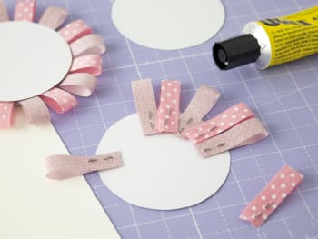 Lavoretti Festa dei Nonni: pinzettare i nastri alle due estremità e applicarli sul cartoncino rotondo come a formare una ghirlanda.