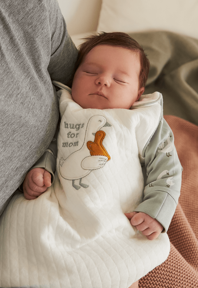 Un bebé con un precioso saco de dormir de patitos duerme relajadamente.