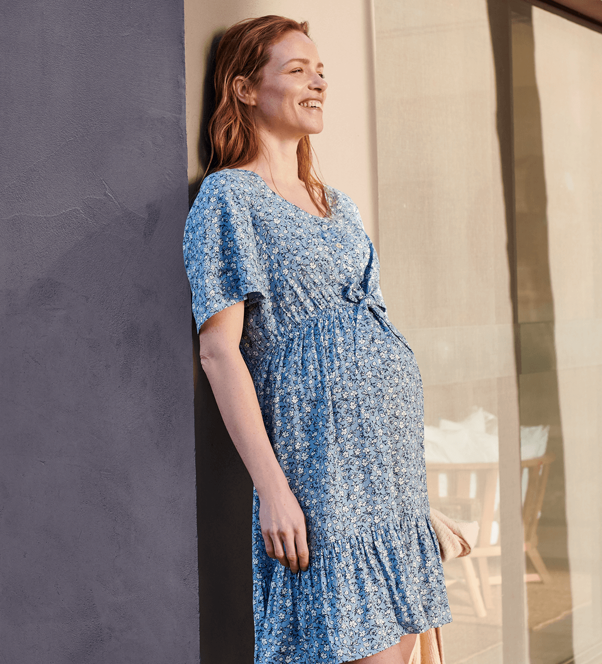 Una embarazada disfruta del sol con un vestido premamá de flores con drapeado por encima de la barriga.