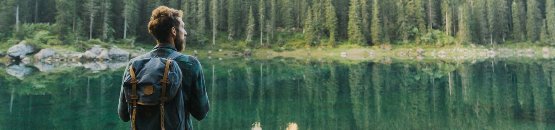 Wędrowiec odpoczywa podziwiając widok na jezioro w górach, otoczone lasem.