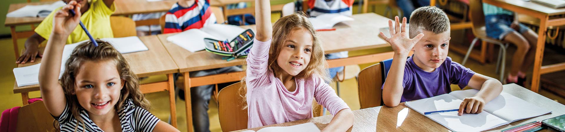 Lagereschooltijd - leerlingen steken hun hand op om de vraag van de leraar te beantwoorden.