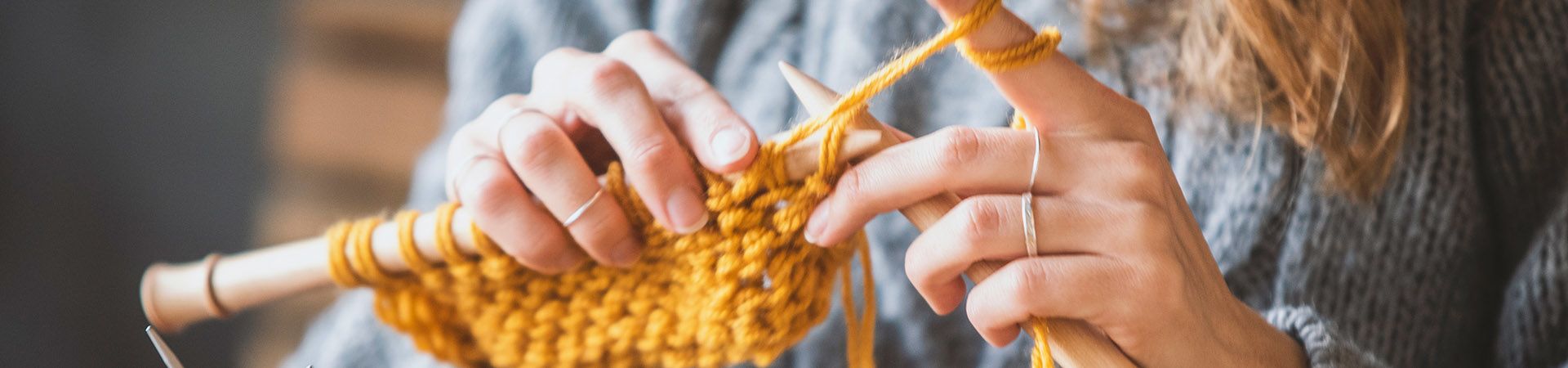 Learning to knit: A woman knitting with yellow wool.